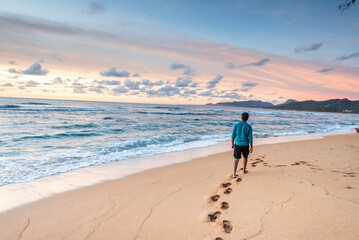 Tourist walking alone on sandy beach at sunset, enjoying beautiful ocean view in kauai, hawaii