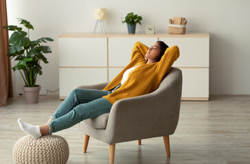 A relaxed Arab woman is sitting in a comfortable armchair with her hands behind her head and eyes...