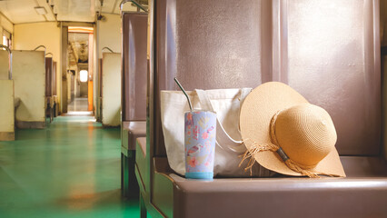Straw hat with tote bag and tumbler placed on vintage train seat, capturing a relaxing travel...