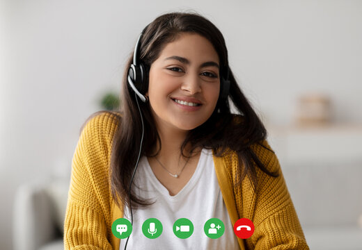 A cheerful arab woman connects with loved ones through a video call. She wears a headset and smiles while using her computer, creating a warm atmosphere for virtual conversations.