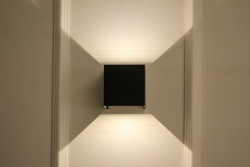 Minimalist wall lamp casting geometric light and shadow patterns on a neutral wall. Perfect for contemporary interior design themes.