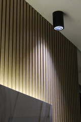 Close-up of a sleek black wall light fixture illuminating a white wall in a minimalist interior, creating elegant contrast and soft ambient lighting.