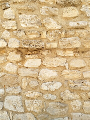 Rustic texture of an old stone wall with uneven, rough, beige and white rocks set in thick, sandy mortar. Vntage, architectural background.