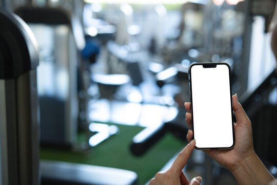 Women hand holding smart phone with blank white screen mockup in gym