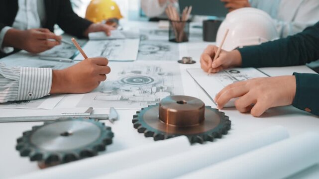 A diverse team of engineers collaborates on project blueprints and technical drawings, surrounded by tools and gear components, emphasizing teamwork and innovation. SACTR