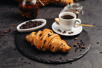 A large airy croissant with chocolate on a dark background tempts coffee