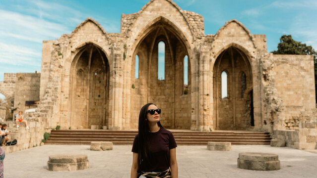 Woman exploring the sensational medieval church ruins in Rhodes, Greece. Ancient architecture, stone walls, and historic atmosphere. Travel and cultural exploration concept.