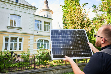 Man holding photovoltaic solar panel in front of historical building. Concept of integration of sustainable renewable energy sources into architecture.