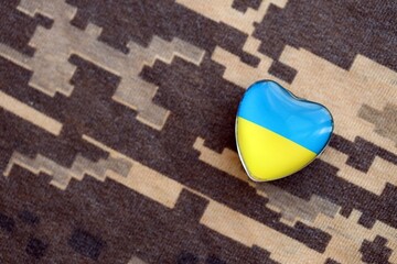 Glass heart with Ukrainian flag lies on military camouflage fabric. Concept of support and defend Ukraine