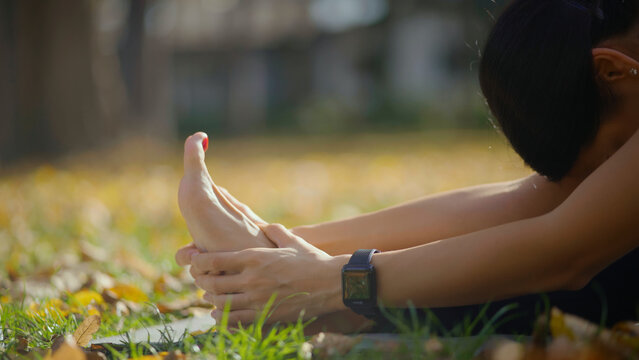 Woman performing a seated forward bend pose in yoga, stretching her back and hamstrings on a mat in a park setting during autumn, promoting wellness and flexibility