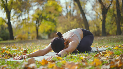 Woman practicing child's pose on a yoga mat in a sunny autumn park, surrounded by golden leaves, embracing calm, mindful stretching and outdoor wellness for body and mind