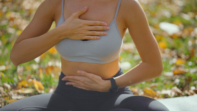 Woman performing breathing exercise outdoors with hands on her chest and abdomen, focusing on wellness and relaxation during a yoga or meditation session in an autumn park