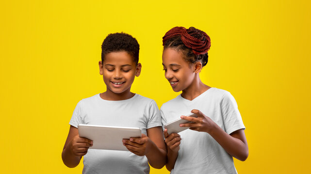 Two children stand side by side, engaged with their devices, sharing smiles and excitement. The vibrant yellow background adds energy to the scene, highlighting their joy in discovering together.