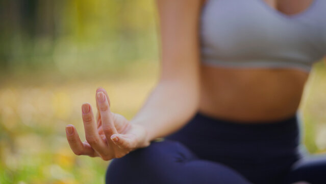 Woman meditating cross-legged in a peaceful park, practicing gyan mudra for inner balance, mindfulness and wellness amid autumn greens, calm focused breath and tranquility