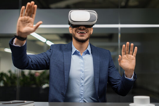 A young businessman wearing VR glasses in the office shows signs of amazement as he gestures in excitement. This scene captures the impact of virtual reality solutions in the workplace.