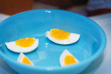 Soft-boiled egg, quartered vertically, served on a blue plastic plate for a child