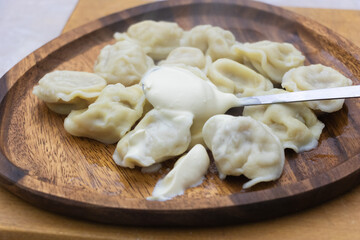 Traditional boiled dumplings served with sour cream on wooden plate, homemade pelmeni food closeup