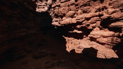 Shadows dance across the sunlit canyon walls as the vibrant red rocks reveal their textures and contours, creating a mesmerizing landscape in a tranquil natural setting.
