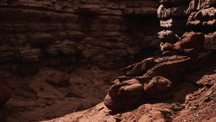 A dramatic canyon landscape features striking red rocks and towering walls under bright sunlight. Shadows enhance the textures and colors of the geological formations, creating an awe inspiring sight.