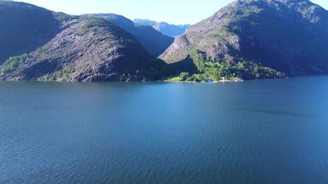 Drone flying straight toward the fjord beside Langfoss in Fj&aelig;ra, capturing steep surrounding mountains and the dramatic Norwegian landscape.