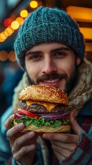 A smiling man holds a large, delicious-looking burger.  He's bundled in winter clothing