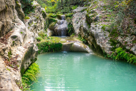 A small waterfall cascades down from mossy rocks into a natural turquoise pool. Dense vegetation, vines, roots, and moss can be seen everywhere. (saklı, gizli cennet şelalesi) Manavgat - Antalya
