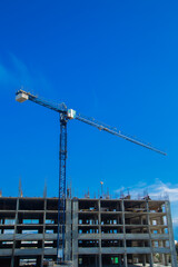 A tall construction crane on a construction site with a clear blue sky and a concrete structure illustrating the dynamic nature of urban development and construction work. Concept of construction