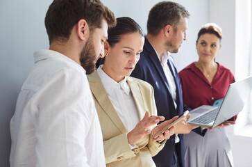Office employees standing discussing online project, showing laptop computer presentation to skilled team leader, friendly diverse colleagues working in pairs using applications, supervisor share