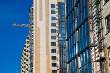 Modern residential buildings are being built with cranes in the foreground against a bright blue sky, highlighting the city's growth and construction activity. High quality photo