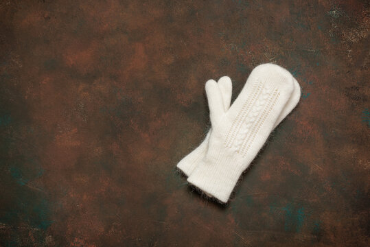 White knitted mittens on dark brown grunge background, top view, flat lay, copy space