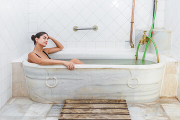 Woman relaxing in a marble bathtub at a thermal spa in a serene environment