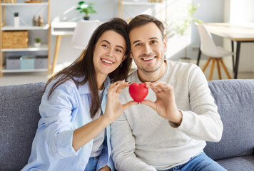 Portrait of a happy family couple holding a red heart. Love and affection are evident as they smile together on Valentine Day, celebrating their relationship and togetherness at home.