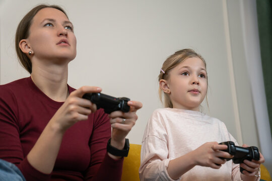 Mother and daughter concentrating while holding game controllers, enjoying a shared video gaming experience and family bonding time together in a domestic setting