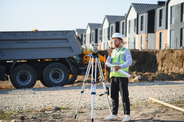 Fototapeta premium Surveyor using theodolite and walkie talkie at construction site