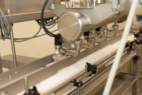 Industrial dispensing nozzles adding marinade or brine into plastic containers filled with herring fillets. Part of an automated seafood packaging system at a modern processing facility.