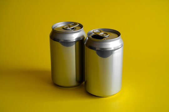 Two silver aluminum cans on a bright yellow background
