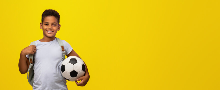 A joyful young boy stands confidently holding a soccer ball under his arm. He wears a simple t-shirt and a backpack, creating a cheerful atmosphere against a vibrant yellow backdrop.