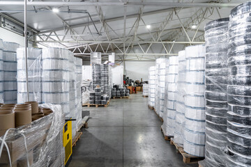 Industrial warehouse with large rolls of packaging film and plastic wrap stacked on pallets. Modern manufacturing, logistics, and material supply chains.