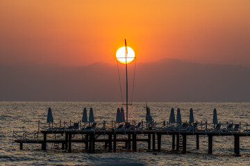 Sunset over an overwater deck with mast framing the sun disk, reflecting on the Mediterranean Sea...