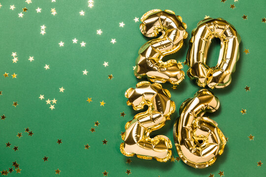 New year 2026 balloon celebration card. Gold foil helium balloon number 2026, party decoration, gold confetti stars on green background. Copy space, flat lay, merry christmas, happy holidays concept.
