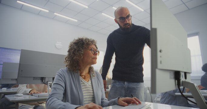 Diverse Mature Students Practice Digital Skills Under Male Teachers Supervision in Bright Computer Class. Concept Inclusion, Upskilling, Continuous Learning, and Digital Empowerment. High Angle.