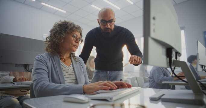 Middle Aged Female Student Works on Computer Project While Teacher Stands Beside, Guiding and Reviewing Progress. Concept Adult Education, Mentoring, Digital Learning, and Professional Development.