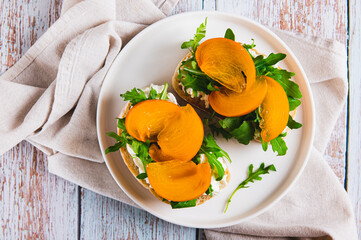 Close up of sandwiches with ricotta, arugula and persimmon on a plate on the table top view