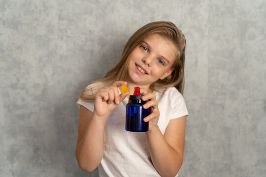 Chewable vitamins for children. A little girl holds in her hands vitamins multicolored chewable bears and a blue jar for them on a gray background. Vitamins and supplements for children. - Powered by Adobe