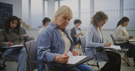 Group Mature Students Works on Written Exercises as Teacher Explains Material. Everyone Sits...