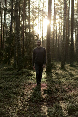 Man walking in a forest at sunset, with sunlight filtering through the trees