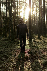 Man walking in a forest at sunset, with sunlight filtering through the trees