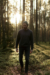 Man walking in a forest at sunset, with sunlight filtering through the trees