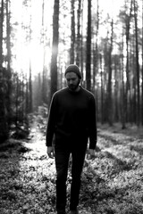 Man walking in a forest at sunset, with sunlight filtering through the trees