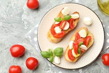 Tasty bruschettas with mozzarella cheese, tomatoes and basil on grey textured table, flat lay